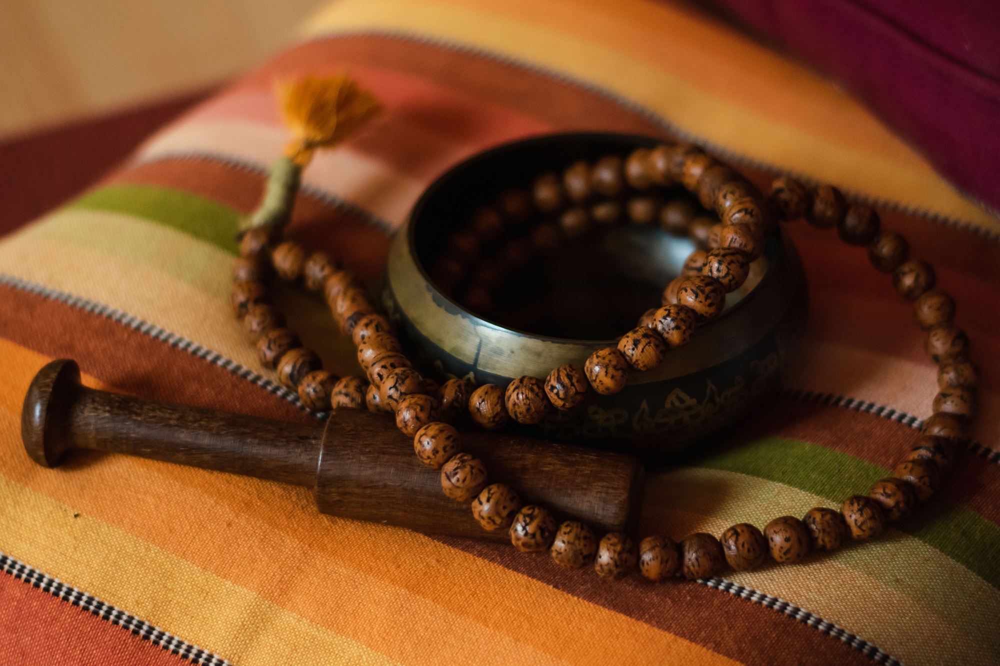 Closeup shot of a Tibetan bowl with a mala on a striped cushion